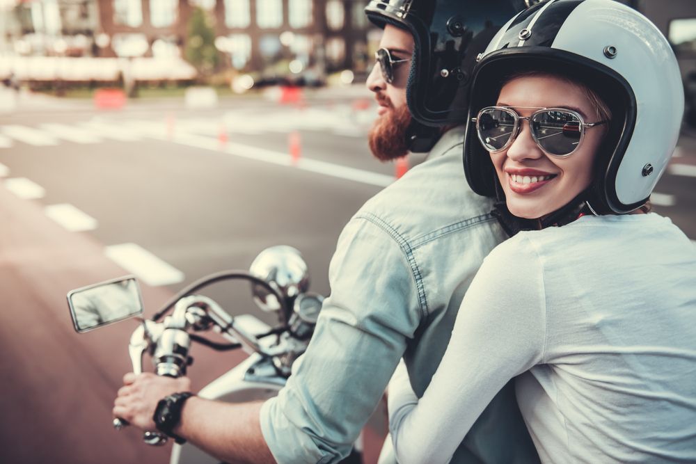 Beautiful young couple in sunglasses and helmets is smiling while riding a motorcycle